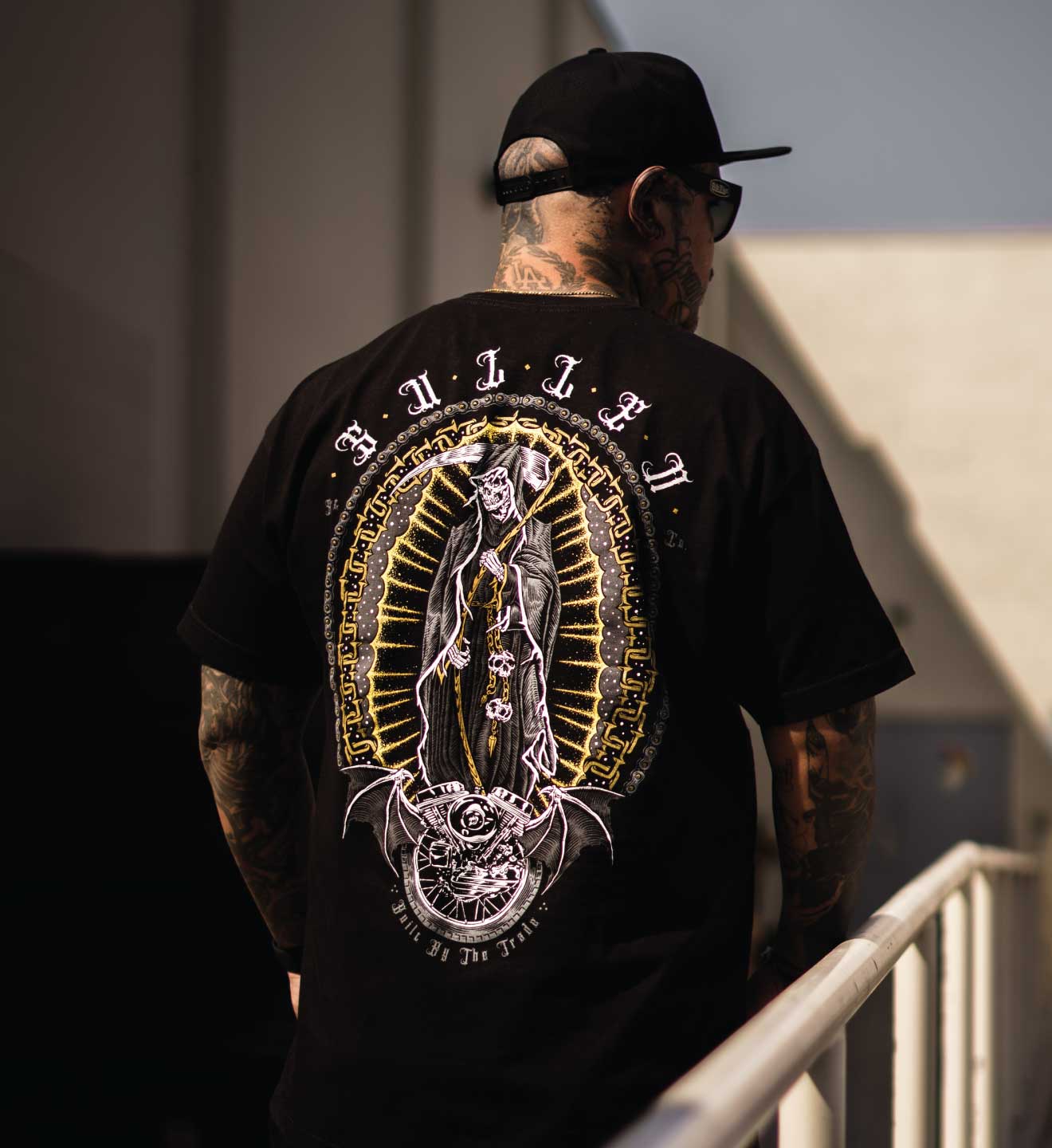 A person wearing a black t-shirt with a graphic design of a skeleton reaper on the back, walking away from the camera.