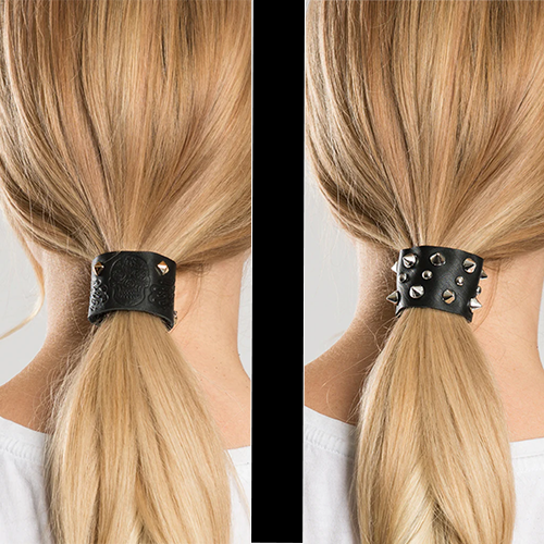 Two ponytail holders, one with deossed skulls and the other with spiked studs, on the hair of a person with blonde hair.