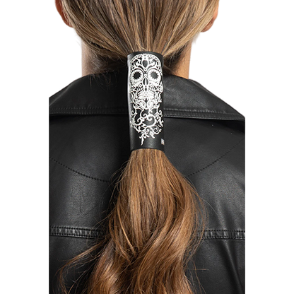 A person with a tribal skull patterned hair glove in black color, worn on a ponytail, against a black leather jacket background.