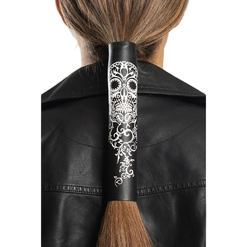 A person wearing a black leather jacket and a ponytail holder with a tribal skull design in white.