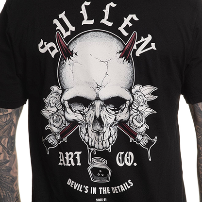 A person wearing a black premium t-shirt with a back graphic of a skull and the text 'Sullen Art Co. Devils in the details'.