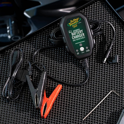 Battery Tender battery charger on a textured black surface with clamps attached.