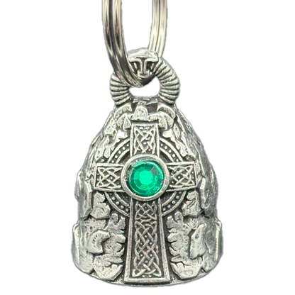 A Celtic cross-shaped motorcycle bell with intricate designs and a green emerald-like center, attached to a silver-colored split ring.
