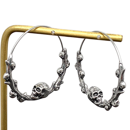 Silver hoop earrings with skull designs on a gold stand against a white background
