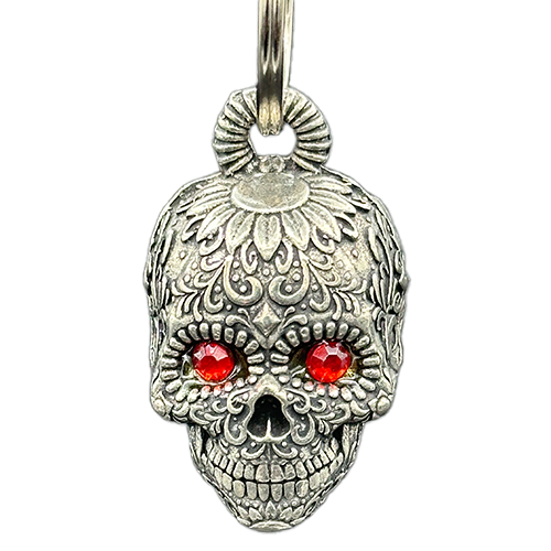 A silver-colored sugar skull bell with intricate designs and ruby-like jeweled eyes, attached to a metal split ring.